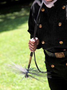 Original of Chimney Sweep with gold buttons going down each side of the shirt and a golden belt buckle. He is holding a sweep brush.